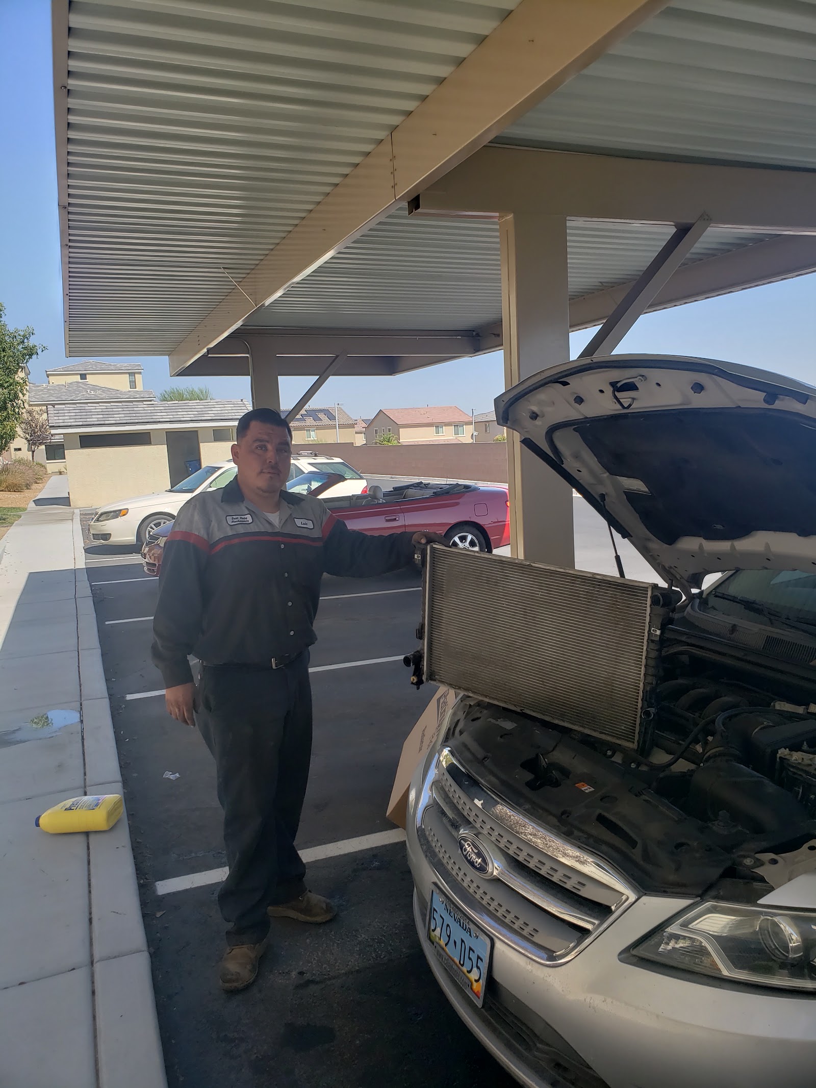 Mobile mechanic in uniform standing beside a white Ford with a new radiator during a repair