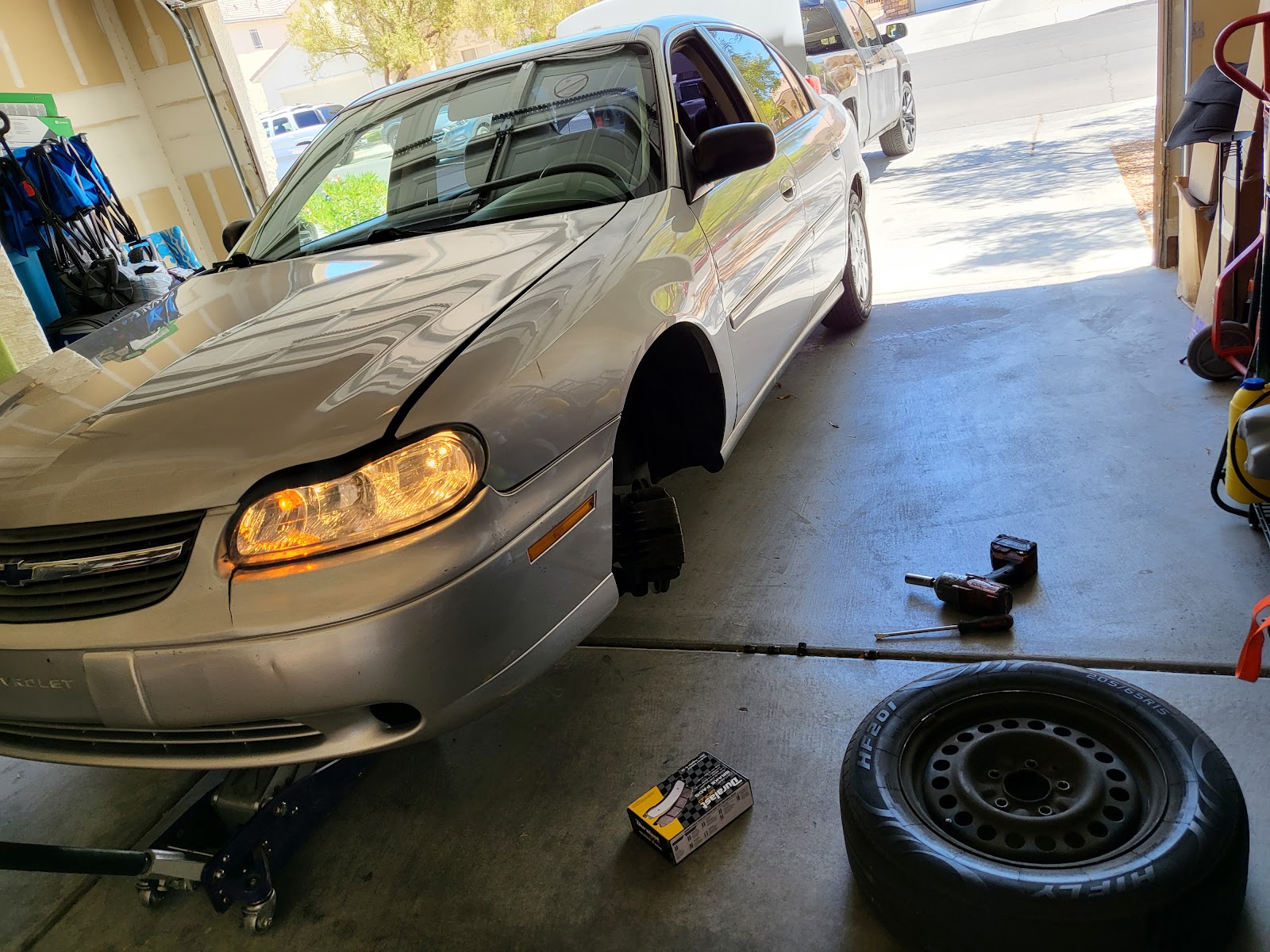 Silver Chevrolet Malibu on a floor jack with wheel removed for brake service in a garage