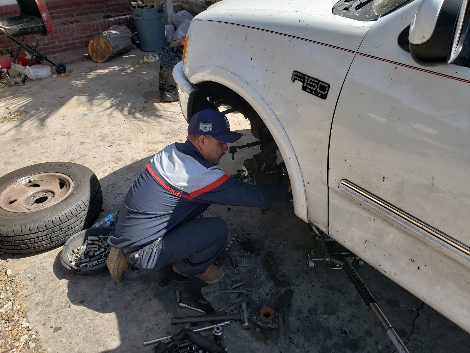 Mechanic kneeling to work on the front suspension of a white Ford F-150